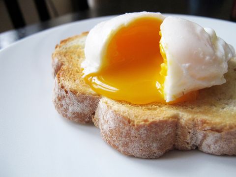 un seul œuf poché sur du pain grillé tranché à la main de manière artisanale l'œuf est divisé pour révéler une assiette blanche au jaune coulant, une table et une chaise en bois sombre à peu près visibles à l'arrière-plan